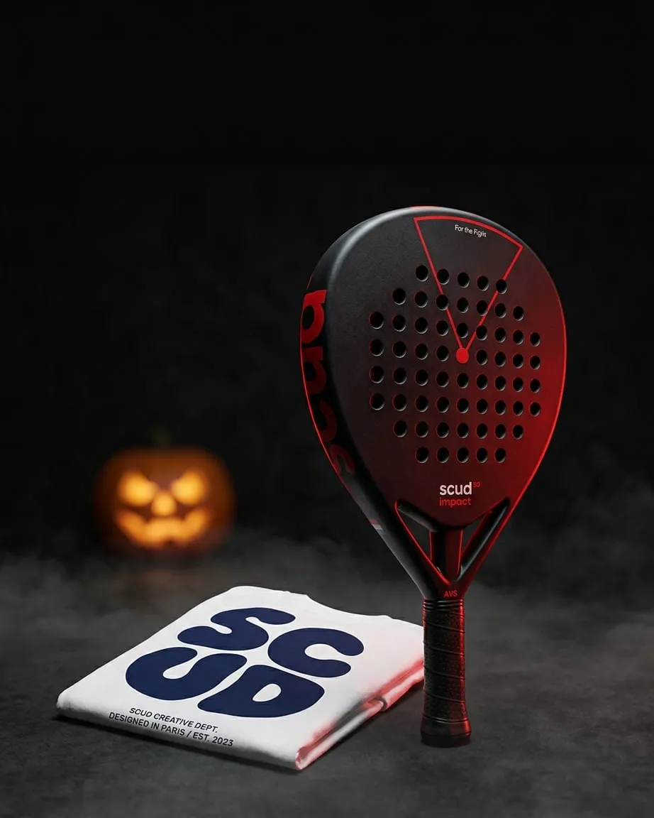 Pack Halloween SCUD mis en scène : la raquette Black Impact B3 debout près du t-shirt SCUD blanc plié, entre des citrouilles éclairées, dans la brume