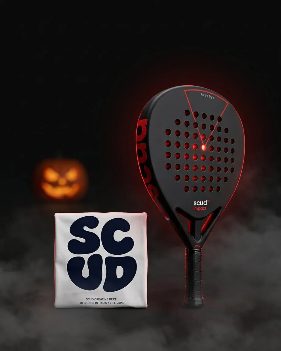 La Black Impact B3 debout dans la brume, sous une lueur rouge, à côté du t-shirt SCUD plié et d'une citrouille d'Halloween