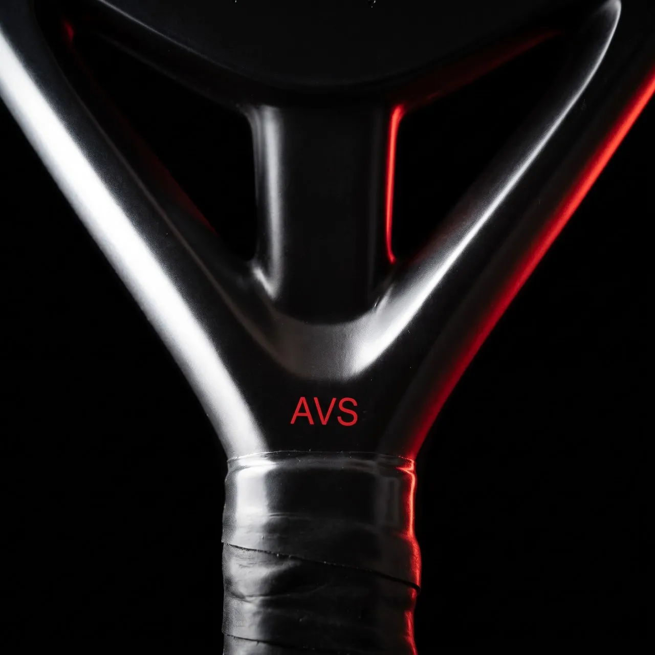 Macro du cœur d'une raquette SCUD : la fourche gunmetal et la marque AVS rouge, juste au-dessus du grip