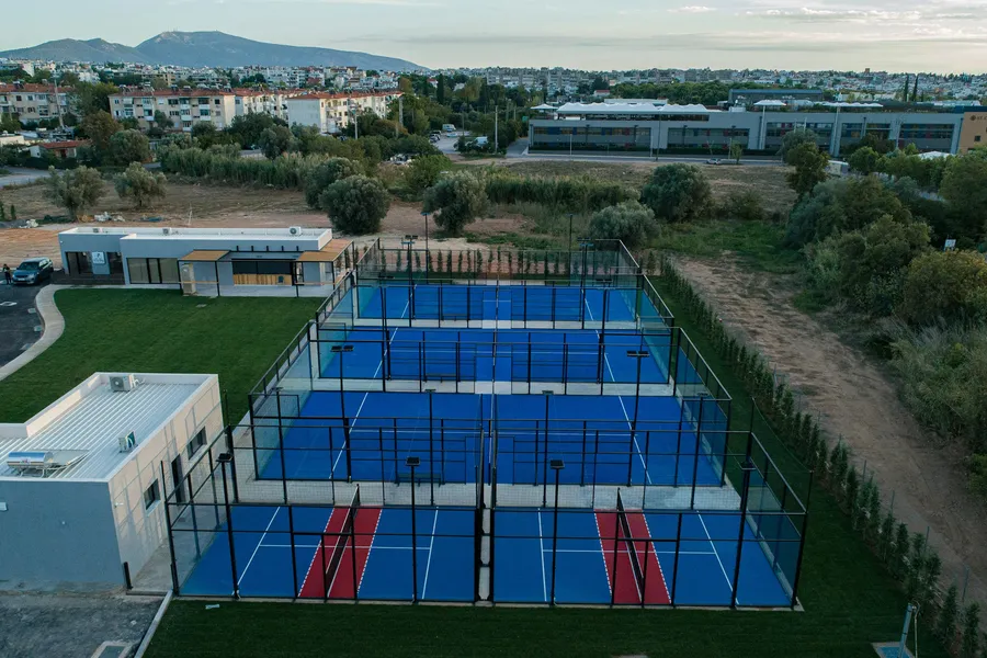 Um clube de padel ao ar livre ao anoitecer: cinco campos de vidro azuis rodeados de vegetação