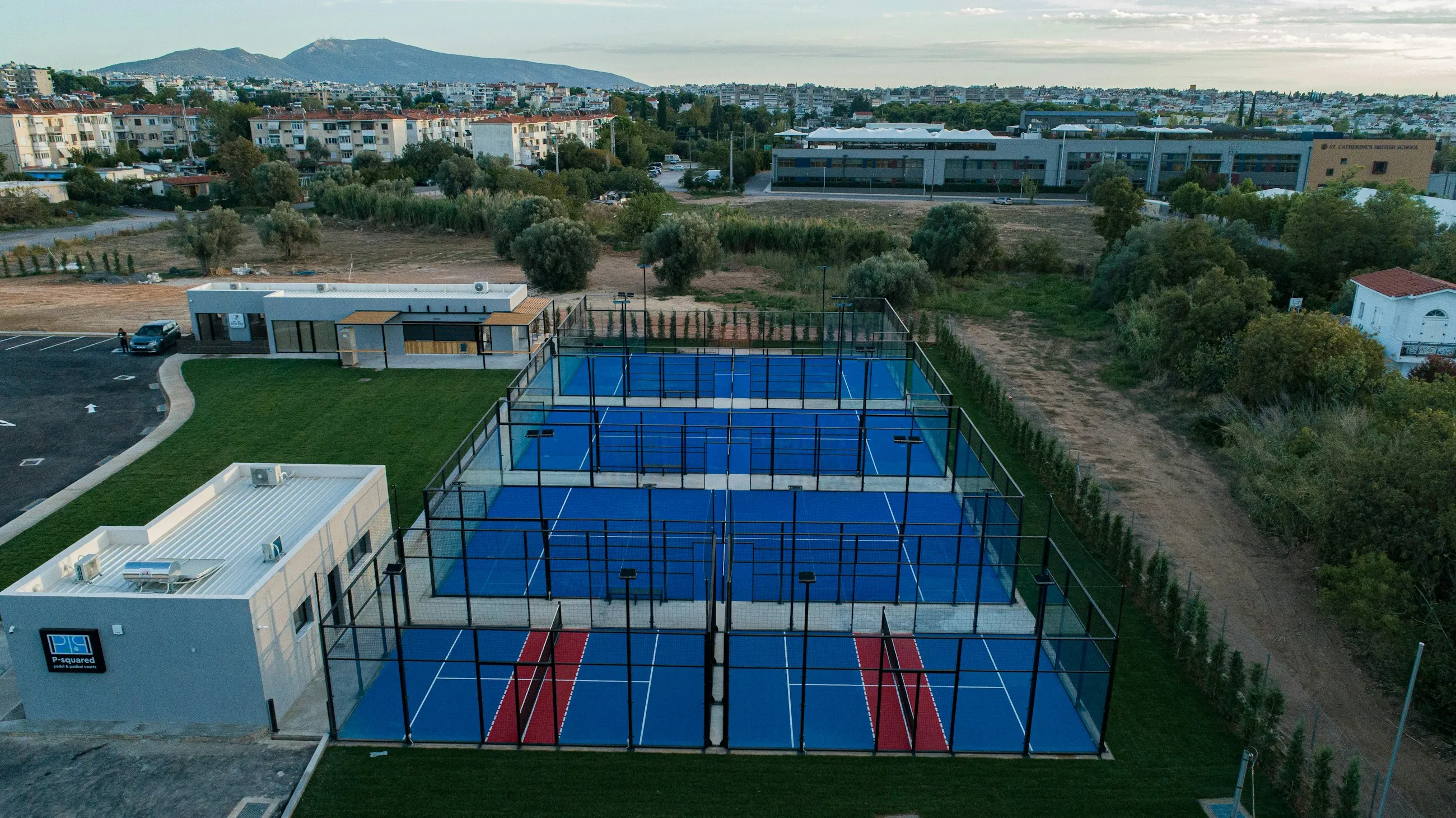 Um clube de padel ao ar livre ao anoitecer: cinco campos de vidro azuis rodeados de vegetação