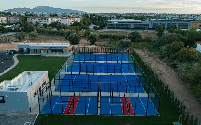 Um clube de padel ao ar livre ao anoitecer: cinco campos de vidro azuis rodeados de vegetação