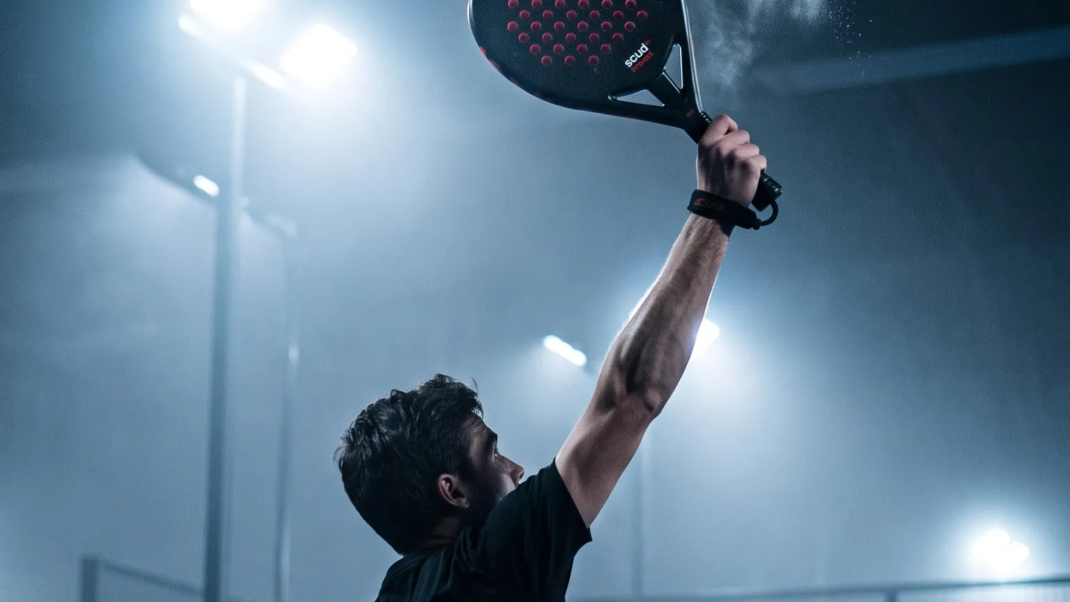 Joueur de padel au smash, raquette SCUD levée, sur un terrain couvert éclairé de nuit