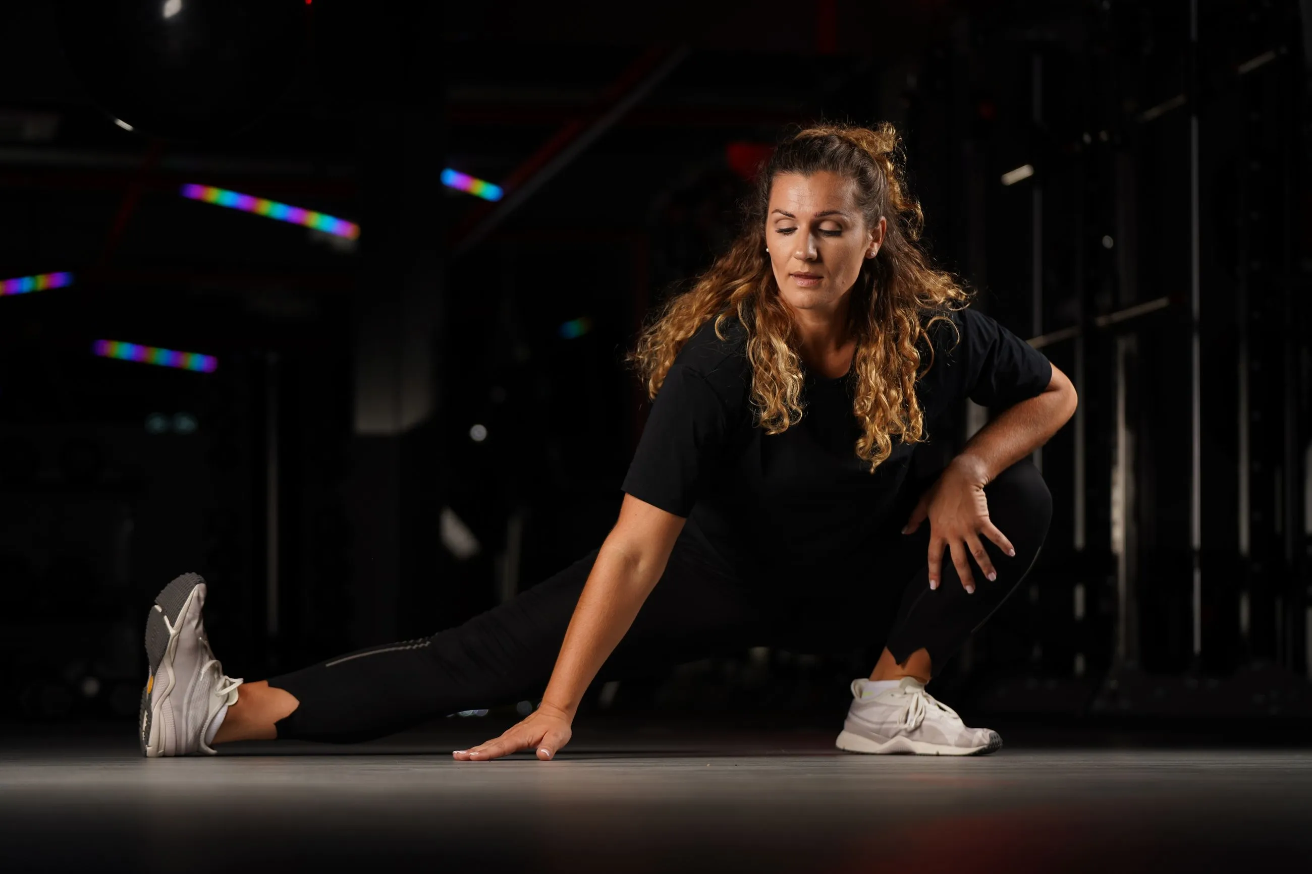Um atleta a alongar-se em afundo lateral, com uma mão no chão, num ginásio escuro