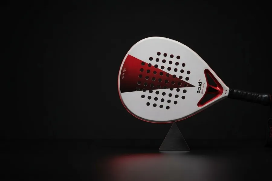 Raquette SCUD White S3 posée à l'horizontale en équilibre sur un pivot d'acier, sur fond noir : le point de balance