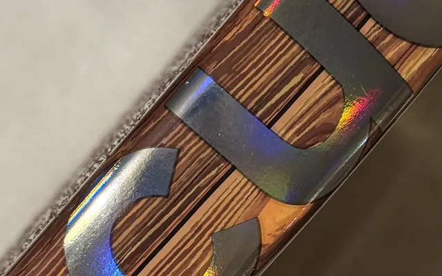 Grande plano do aro da SCUD Wood W1: acabamento em madeira e letras holográficas