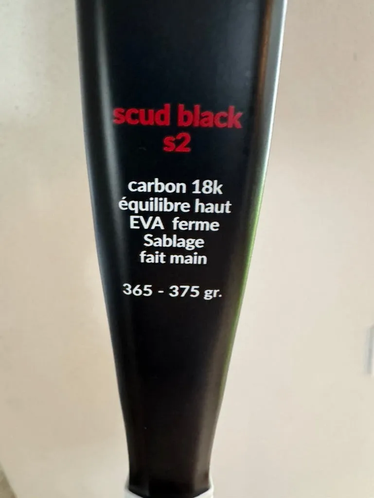 Gros plan du cadre d'une raquette de padel SCUD noire : « scud black s2 — carbon 18k, équilibre haut, EVA ferme, sablage fait main, 365-375 gr » imprimé sous le cœur