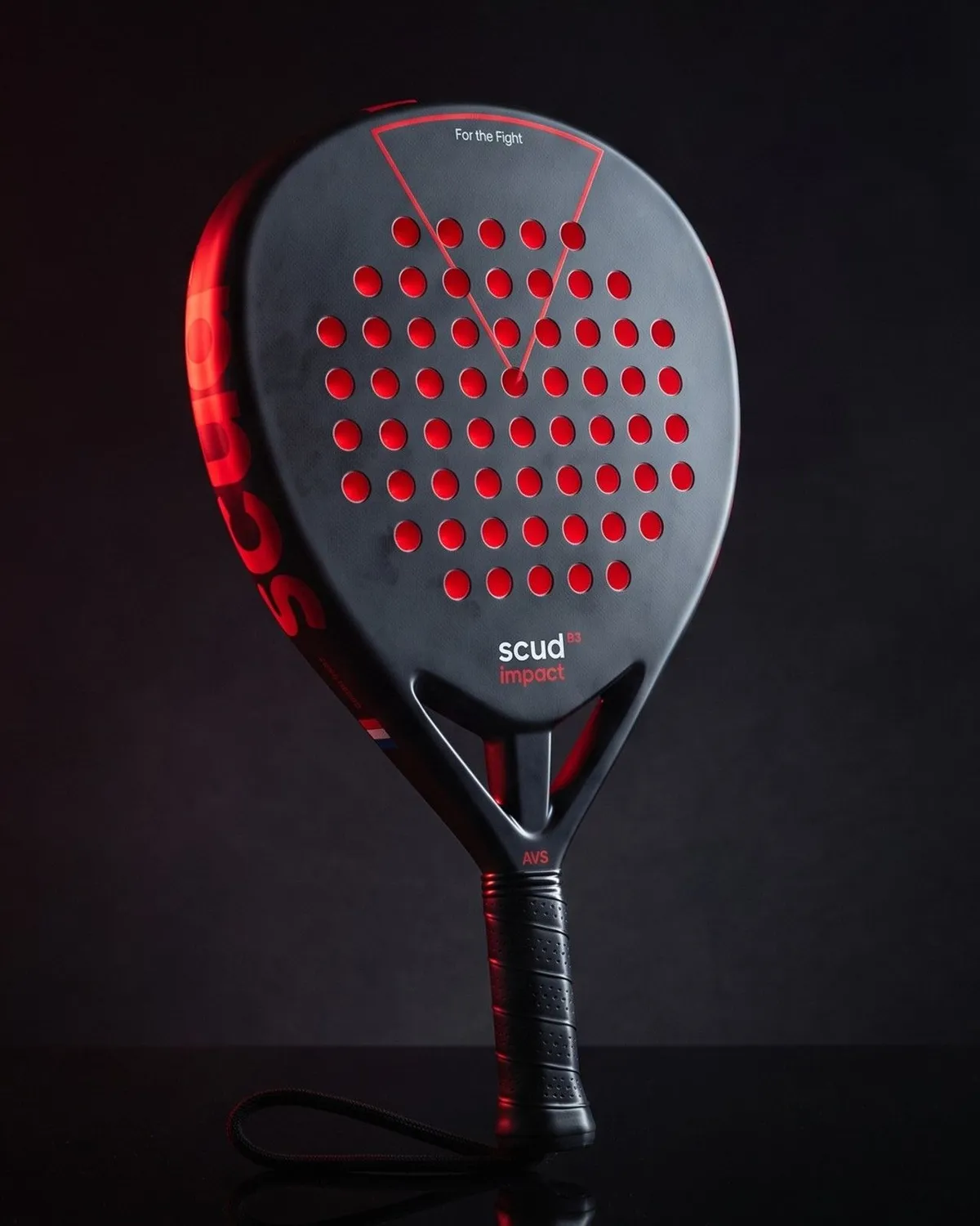 La Black Impact B3 de pie en la penumbra, una luz roja sobre su marco marcado scud, la cara negra perforada en rojo reflejada en un suelo negro