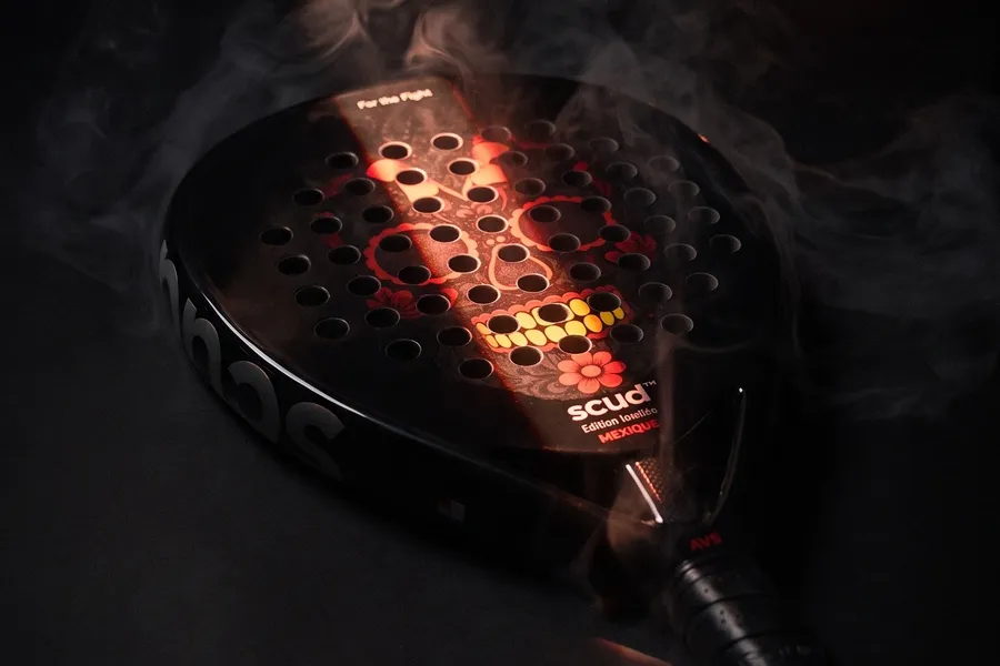 Raquete SCUD Black Impact B3 deitada no fumo, à luz de velas, com as perfurações vermelhas a brilhar
