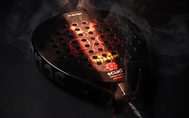 Raquete SCUD Black Impact B3 deitada no fumo, à luz de velas, com as perfurações vermelhas a brilhar
