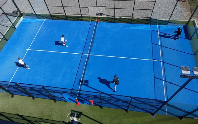 Quatro jogadores num jogo de pares num campo de padel azul ao sol, vistos de cima