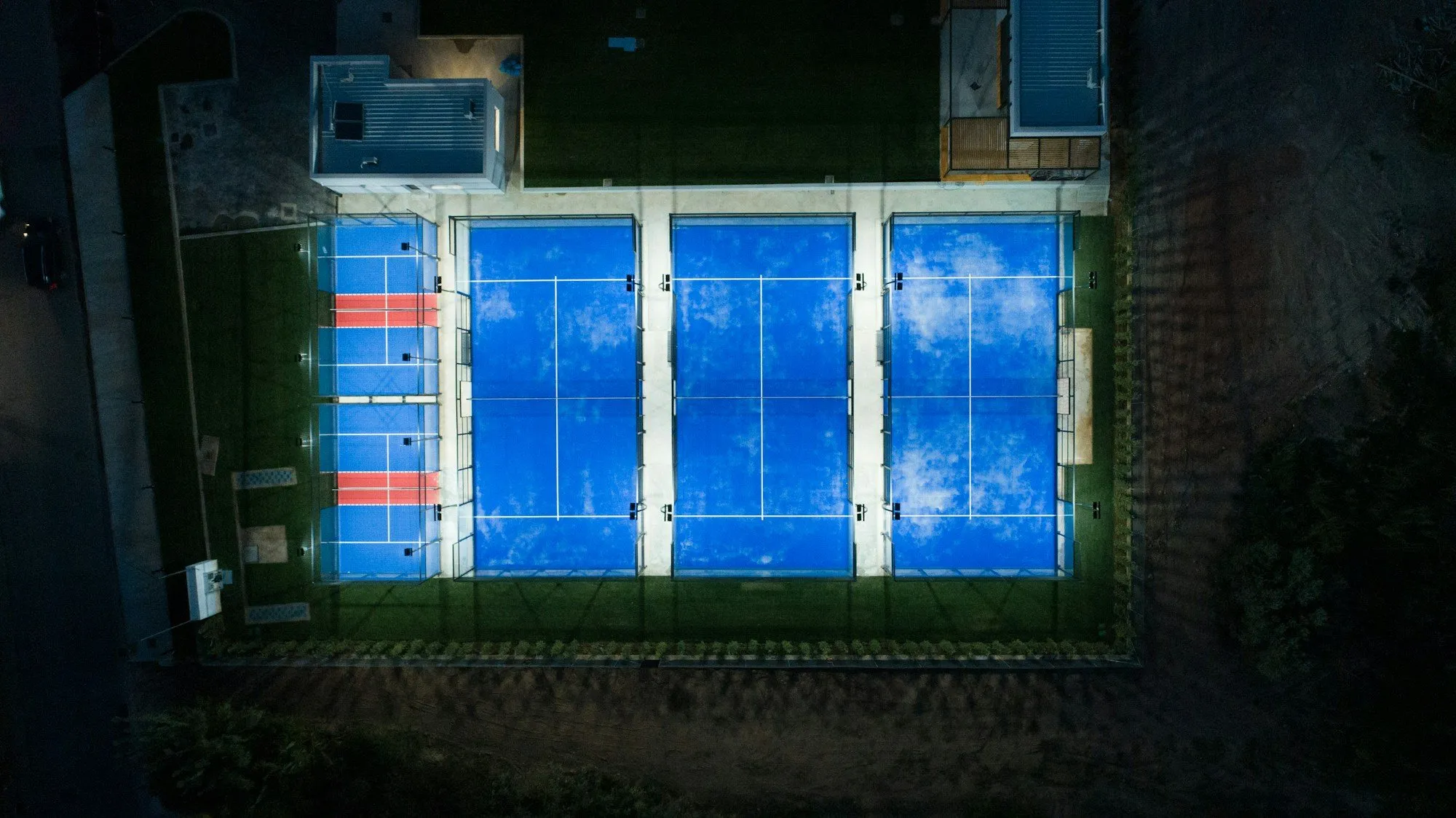 Três campos de padel iluminados à noite, vistos de cima