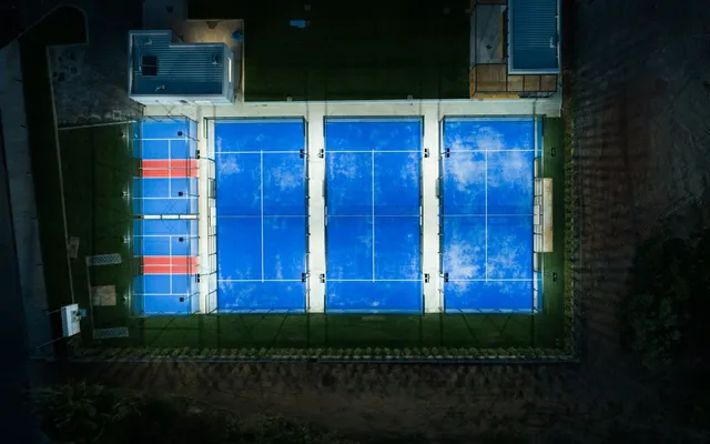 Três campos de padel iluminados à noite, vistos de cima