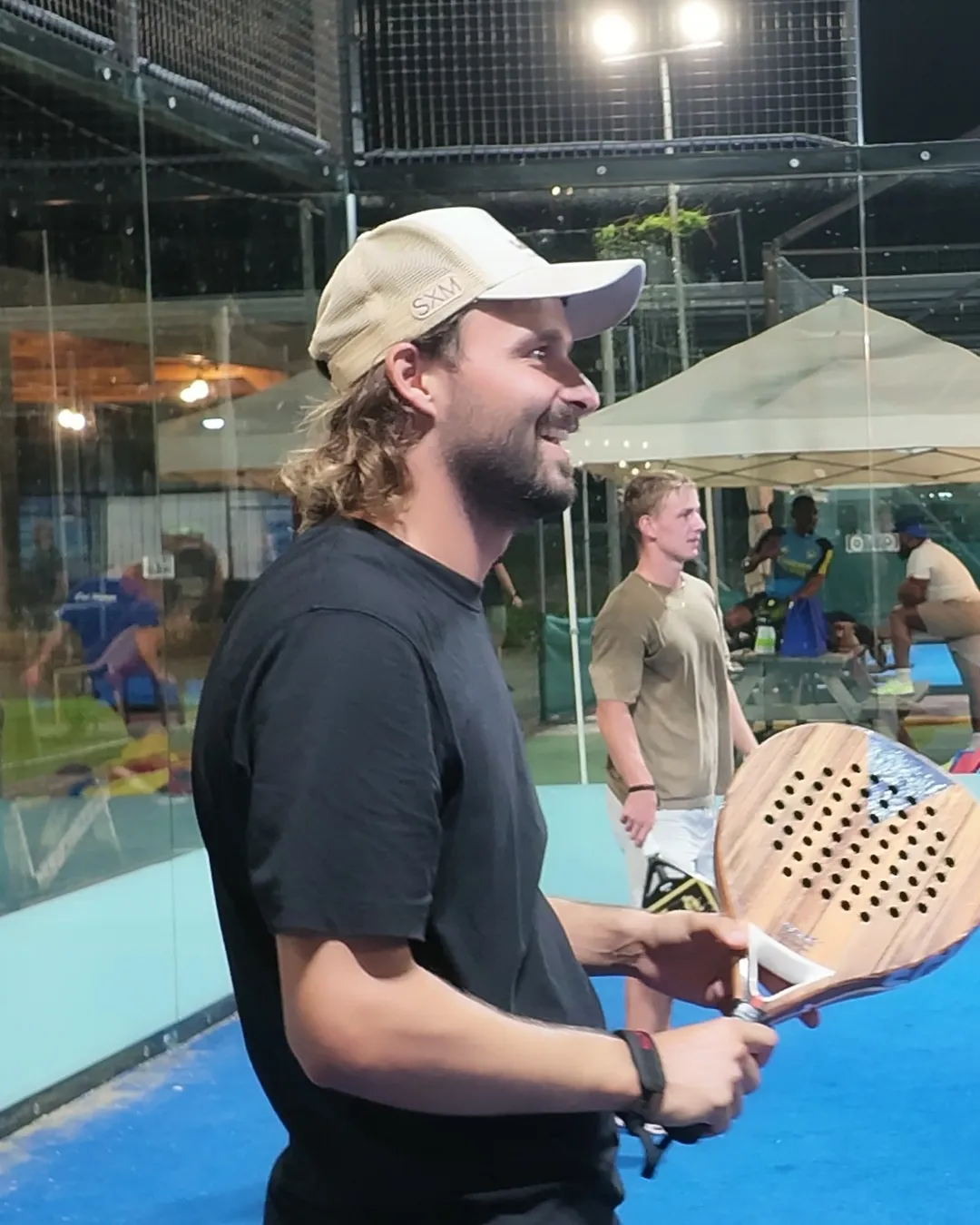 Un joueur à casquette sourit, raquette SCUD Wood en main